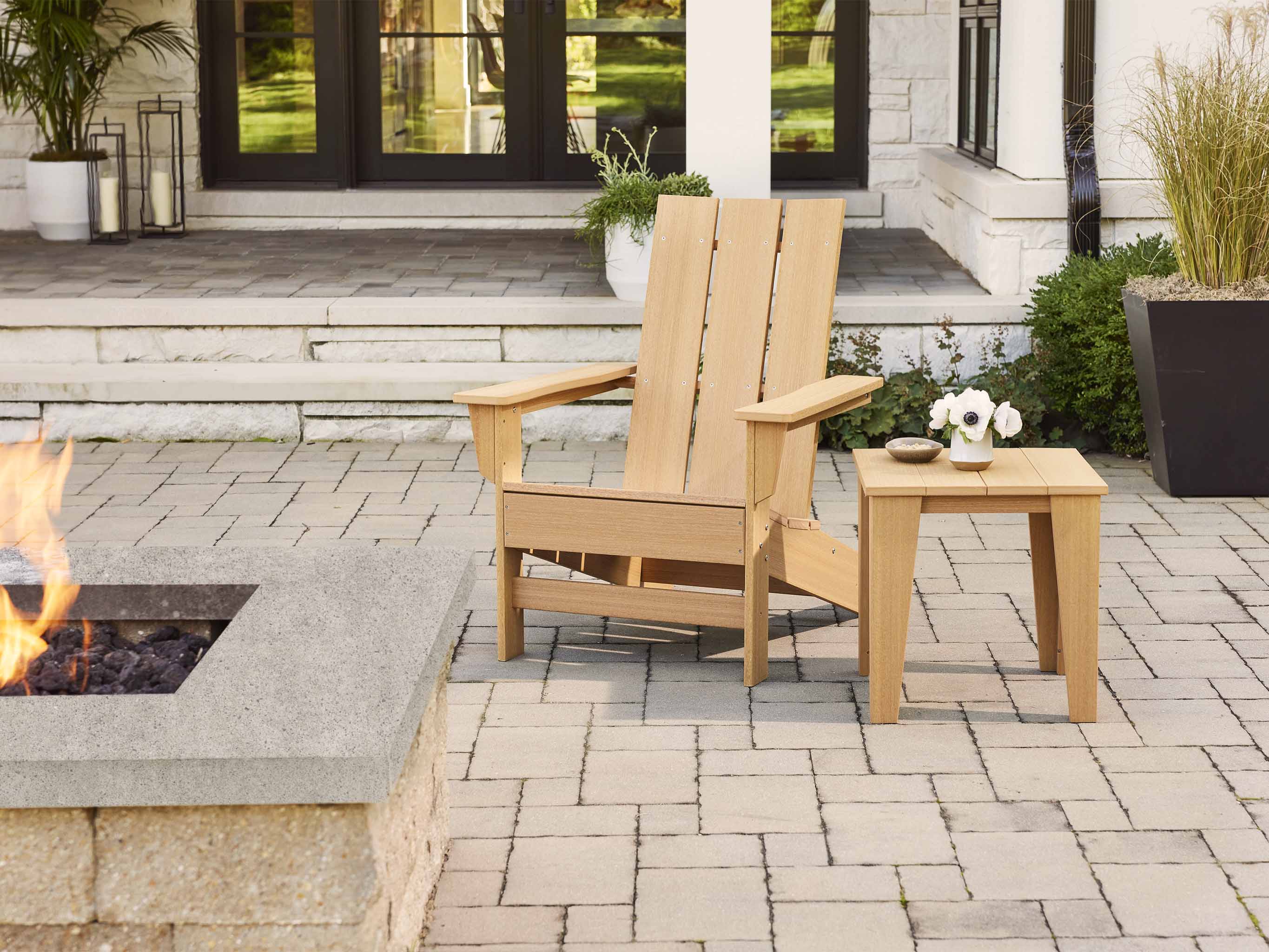 Aria Natural Teak Adirondack Chair and Modern Side Table on brick patio next to a fire pit